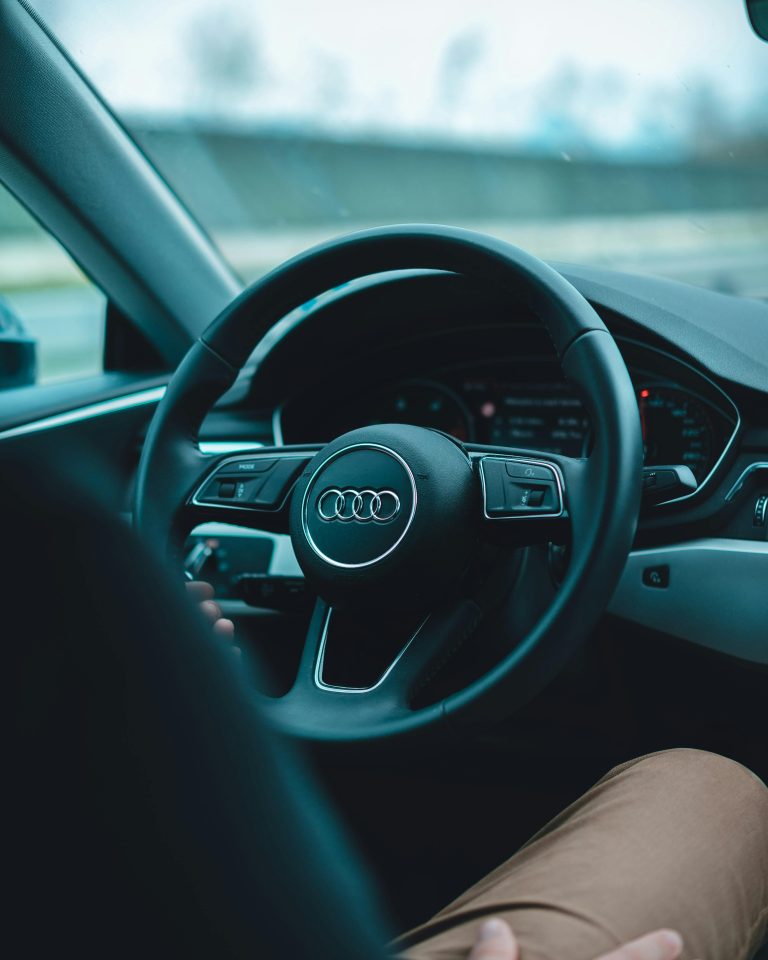 Interior view of a man driving an Audi with focus on steering wheel and dashboard.