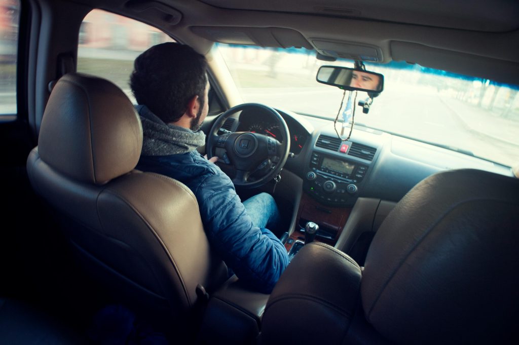 A man driving a car with focus on interior, dashboard, and steering wheel, captured from the backseat.